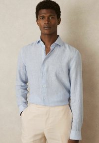 Himmelblau gestreiftes Button-Down-Hemd aus Baumwollstoff, mit klassischem Kragen und langen Ärmeln, kombiniert mit hellen Hosen.