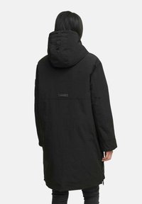 Parka noire longue avec capuche, en tissu texturé, dotée d'un cordon de serrage ajustable et d'un patch logo au dos. Design simple.
