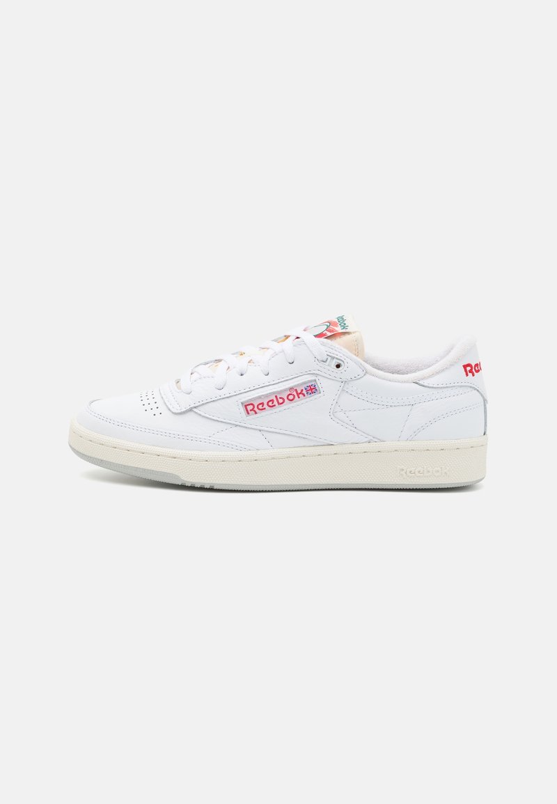 Baskets en cuir blanc avec un bout perforé, un laçage à l'avant et un logo Reebok rouge. Elles présentent une semelle en caoutchouc crème et des détails colorés au niveau du talon.