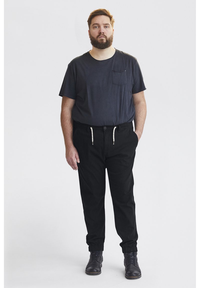 Pantalons noirs avec des poignets élastiques, une taille à cordon de serrage et des poches latérales, associés à un t-shirt ajusté bleu marine avec une poche poitrine.