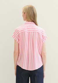 Button-up shirt in pink and white vertical stripes, short sleeves, relaxed fit, rounded hem, and soft fabric. Paired with dark blue pants.