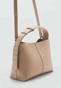 Bolso de hombro de cuero beige con un diseño estructurado, que cuenta con una correa ancha con orificios ajustables y acentos de hardware en plata.