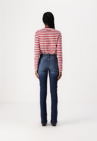 Striped long-sleeve shirt in red and white, with back logo, paired with dark blue fitted denim jeans featuring back pockets.
