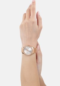 Roségoldene Armbanduhr mit rundem Ziffernblatt, silbernem Zifferblatt, römischen Ziffern und einem diamantähnlich besetzten Lünette. Metallgliederarmband.