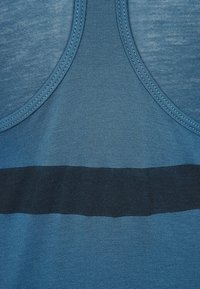 Ärmlös blå tanktopp med en texturerad yta, med ett horisontellt mörkblått rand över midjan. Slät tyg, rund halsringning.