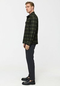Green plaid flannel shirt with a collar, buttoned pocket, and long sleeves, paired with dark gray pants and black shoes.