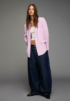 Svetle fialový oversize blazer, bílý zkrácený top a volné tmavé džíny s pěti knoflíky, doplněné černými špičatými botami.