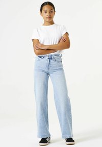 Lichtblauwe, hooggetailleerde jeans met een ontspannen pasvorm en rechte pijp. Gecombineerd met een wit T-shirt met korte mouwen en zwarte sneakers.