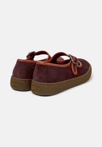 Bordeauxsuede skor med en texturerad brun sula, prydda med ett framträdande orange band med en metalldetalj. Slät yta och böjd design.