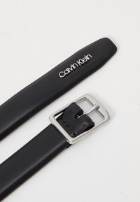 Zwarte leren riem met een rechthoekige zilveren metalen gesp en het reliëf "Calvin Klein" logo op de band. Gladde textuur en gestroomlijnd ontwerp.