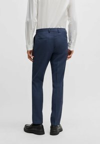 Marineblaue Anzughosen mit feinem Karomuster, geradem Schnitt und Gesäßtaschen, aus strukturiertem Stoff. Sichtbar sind schwarze Schuhe.