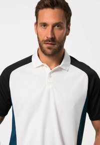 Polo avec un corps blanc, des manches courtes noires et des accents bleu sarcelle. Comprend un col et un logo discret sur la poitrine. Tissu texturé.