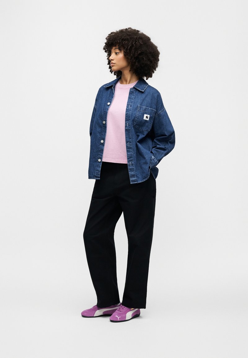Denim jacket with a front pocket, light pink T-shirt, black trousers, and purple sneakers. Features include a button front and relaxed fit.