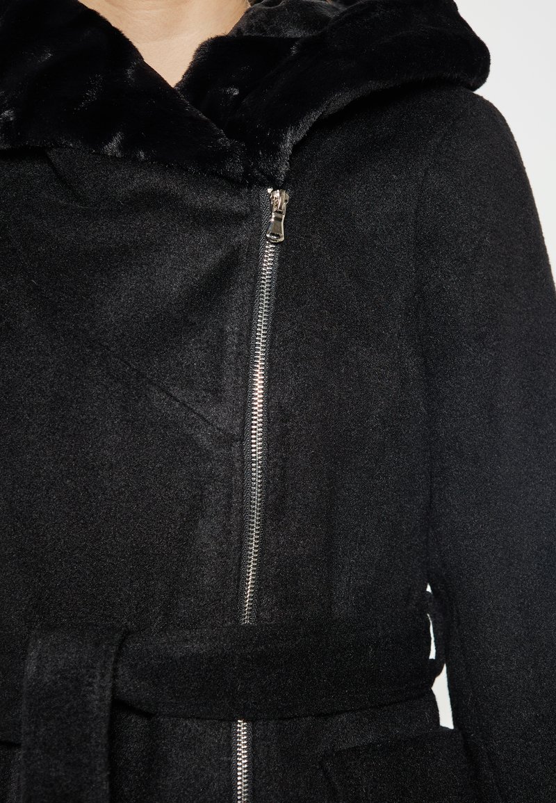 Schwarzer Mantel mit Kapuze aus Kunstfell, Reißverschluss und einem Stoffgürtel in der Taille. Das Material hat ein weiches, strukturiertes Aussehen.