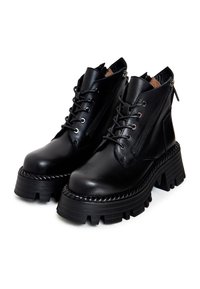 Paire de bottines noires en cuir avec semelles épaisses et massives, lacets à l'avant, fermetures éclair latérales et semelles texturées sur les plateformes.