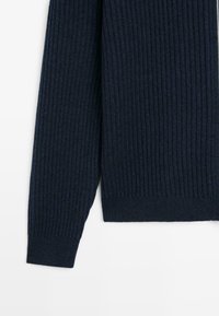 Maglione blu scuro a coste con maniche lunghe e orlo aderente. La texture è morbida e spessa, offrendo un aspetto caldo.