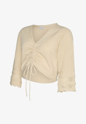 Kremowy, dziergany krótki sweter z marszczonym wiązaniem z przodu, rękawami typu dzwonek o długości 3/4 oraz koronkowymi mankietami z falbanką.