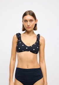 Juodas bikini viršus su baltu gėlių raštu, turi raukšlėtų petnešų, apvalų iškirpimą ir lygų audinio paviršių. Suderintas su aukštu juosmeniu. 