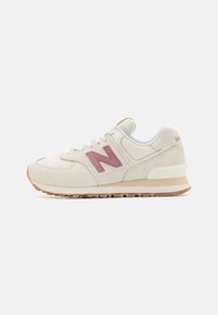 Baskets en daim crème avec des accents rose clair, lacets blancs et une semelle en caoutchouc brun clair. Présente un logo 'N' prominent sur le côté.