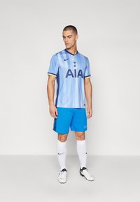 Lyseblåt fodboldtrøje med lodrette striber, marineblå detaljer og teksten "AIA". Sammen med klare blå shorts og hvide sokker. Nike-logoet er synligt.