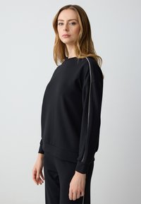Black sweatshirt with round neckline, long sleeves, and ribbed cuffs. Features silver side stripe for accent. Soft, textured fabric.