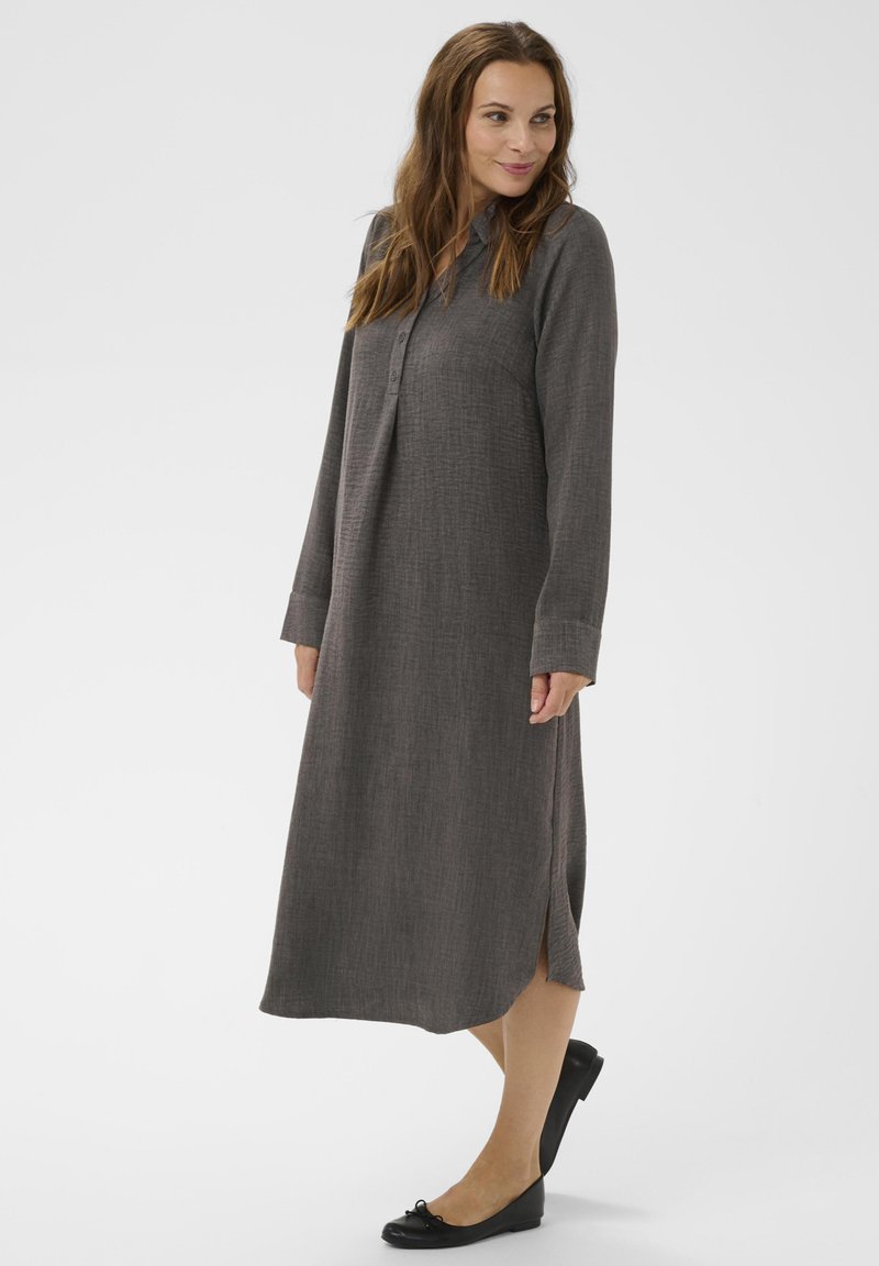 Robe grise à manches longues en tissu texturé, avec un col à boutons et des fentes sur les côtés, associée à des ballerines noires.