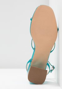 Sandaalit korkealla korolla turkoosina, joissa on sileä synteettinen päällinen, avoin varvas, ohuet hihnat ja teksturoitu kumipohja. Koko merkittynä 37.