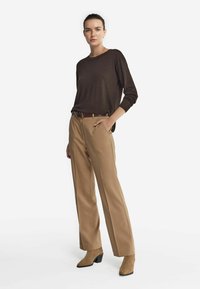 Brauner Strickpullover, beiger hoch taillierter Hosen und kastanienbraune Ankle-Boots mit kleinem Absatz. Einfaches Design mit lockerer Passform und subtilen Texturen.