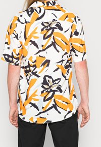 Short-sleeve shirt in white fabric with a large orange and black floral pattern. Relaxed fit with a straight hem and spread collar.