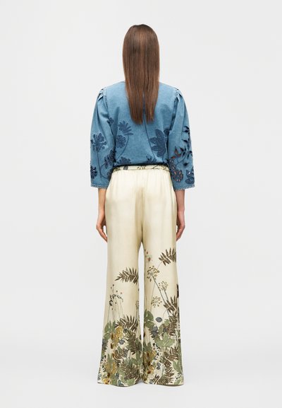 Τζιν μπλούζα με κεντήματα λουλουδιών στα μανίκια και φαρδιά κρεμ παντελόνια με βοτανικό σχέδιο στο τελείωμα. Άτομο που φαίνεται από πίσω.