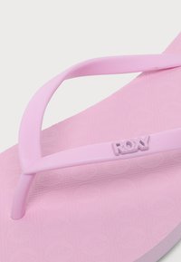 Gros plan d'une sandale tongs rose de la marque Roxy avec une semelle texturée et des brides en caoutchouc simples.