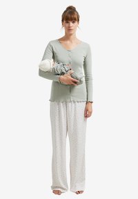 Light green long-sleeve top with button closure, paired with loose-fitting cream pajama pants featuring a floral pattern. Person holds a doll.