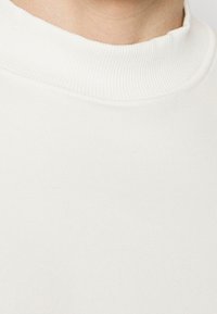 Maglione bianco girocollo con collo spesso a coste, texture morbida e superficie liscia; senza motivi o dettagli hardware visibili.