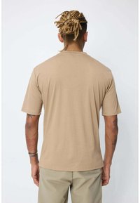 T-shirt beige à manches courtes en tissu doux, avec un col rond et une coupe décontractée. Texture lisse ; design minimaliste sans ornements.