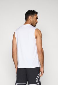 Débardeur de sport blanc sans manches avec un col rond, une texture lisse et une coupe décontractée, associé à un short noir avec des accents blancs.