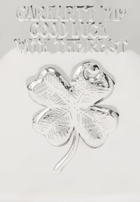 Porte-clés en métal argenté avec un design de trèfle à quatre feuilles, détail gravé et texte indiquant "CARHARTT WIP GOOD LUCK WITH THE REST."