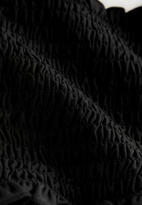 Schwarzer Stoff mit einer strukturierten, gerafften Optik und vertikalen Falten, der Flexibilität und Elastizität in einer Nahaufnahme zeigt.