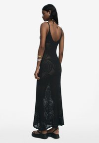 Black crochet maxi dress with a scoop back, featuring a geometric pattern and slim straps. Worn with chunky black sandals.