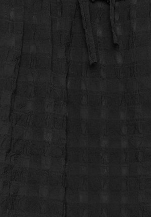 Tessuto nero testurizzato con un motivo a griglia, dotato di vita arricciata e coulisse. La texture sembra leggermente stropicciata e stratificata.