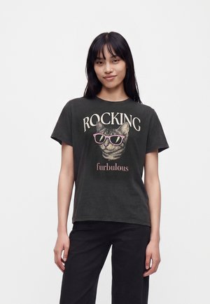 Jeune femme portant un t-shirt noir avec un chat portant des lunettes de soleil roses et les mots "Rocking furbulous" sur le devant.