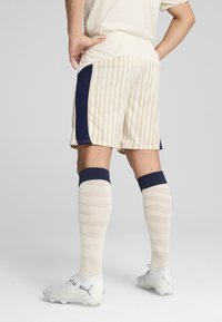 Pantalones cortos a rayas beige y crema con un acento en azul marino, combinados con calcetines de color marrón claro con un patrón en zigzag y zapatillas blancas.