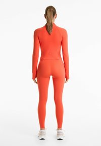 Strakke sportkleding in feloranje, gemaakt van textuurstof met rek. Lange mouwen en bijpassende leggings met een subtiele logodetail.