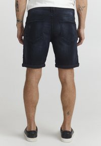 Traperica kratke hlače u tamnoplavoj boji, s preokrenutim rubovima, sa dva stražnja džepa i glatkom teksturom. Nosile su se s crnim slip-on cipelama.