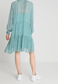 Světle modré dlouhé šaty s vrstvenou sukni, s květinovým vzorem a jemnou, průhlednou tkaninou. V kombinaci s bílými teniskami.