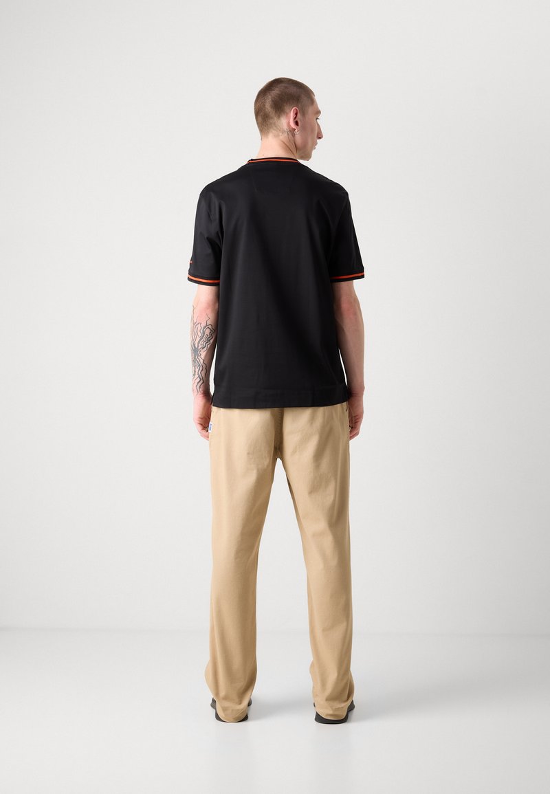 Polo noir avec des accents orange, associé à un pantalon beige ample. Design simple, texture lisse et manches courtes.