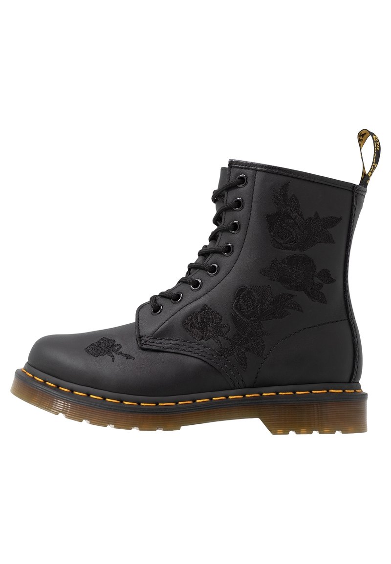 Botte montante en cuir noir avec motifs de roses en relief, couture jaune autour de la semelle et semelle extérieure en caoutchouc translucide marron.