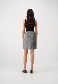 Top noir sans manches avec une jupe en tweed gris, dotée de deux poches arrière, d'une forme structurée et d'une longueur au genou. Chaussures à talons blocs noires.