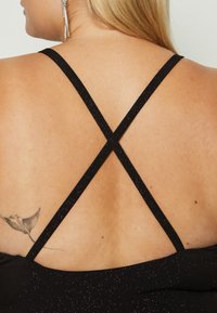 Black dress with thin, sparkly straps crossed at the back. Skin tone visible with a tattoo of a stingray on the lower back.