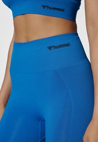 Blå atletisk crop top och högmidjade leggings gjorda av ett smidigt, elastiskt tyg; har logotyp i svart, med subtil textur på leggings.