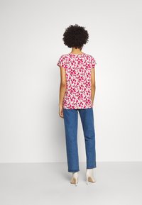 Blommönstrad topp i rosa nyanser; korta ärmar, rund halsringning. Matchad med blå denimbyxor och beiga högklackade skor. Klar bakgrund.